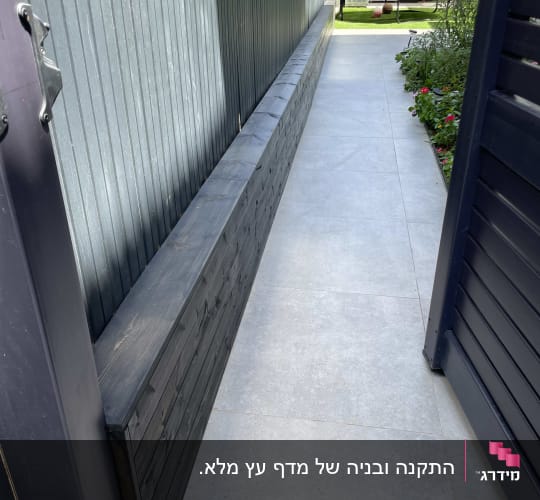גדר עץ כהה לצד שביל מרוצף בגינה